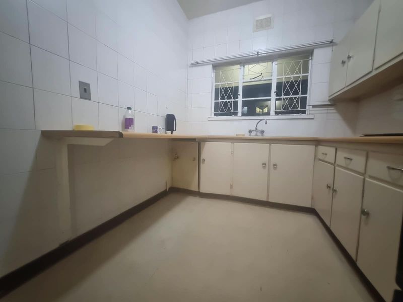 A dated kitchen featuring laminate countertops, built-in cabinetry, and a tiled splashback, offering a blank canvas for potential renovation and modernization.