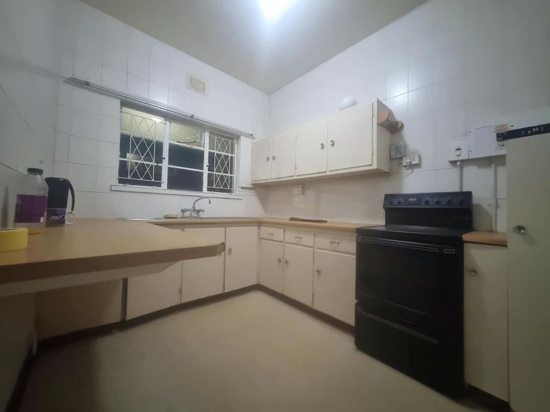 A functional kitchen featuring dated cabinetry, laminate countertops, tiled walls, and a freestanding stove, offering potential for a modern renovation.