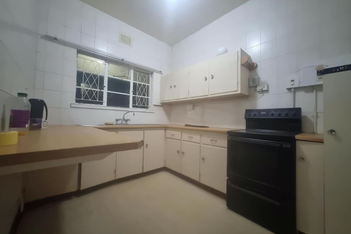A functional kitchen featuring dated cabinetry, laminate countertops, tiled walls, and a freestanding stove, offering potential for a modern renovation.