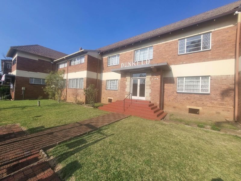Front elevation of the Dunkeld apartment complex featuring classic brick architecture, a tiled roof, and a landscaped front garden area.