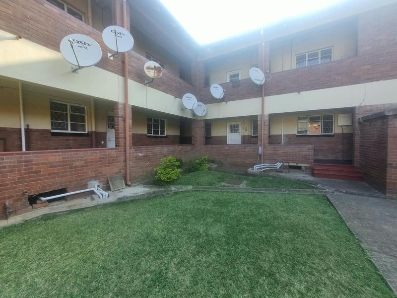 Rear view of a multi-story apartment complex featuring brick facade, communal lawn area, and multiple satellite dish installations.