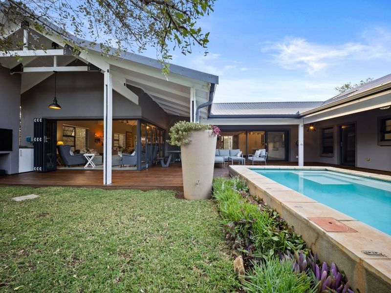 A beautifully landscaped outdoor area featuring a swimming pool, timber decking, and a spacious covered patio with seamless indoor-outdoor flow.