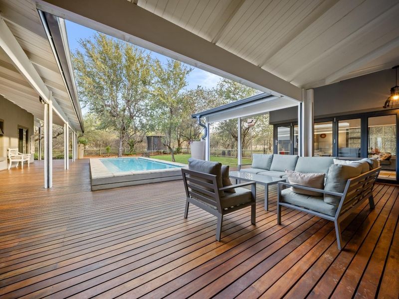 Spacious covered timber deck patio overlooking a private swimming pool and landscaped garden, featuring seamless indoor-outdoor flow through large sliding glass doors.