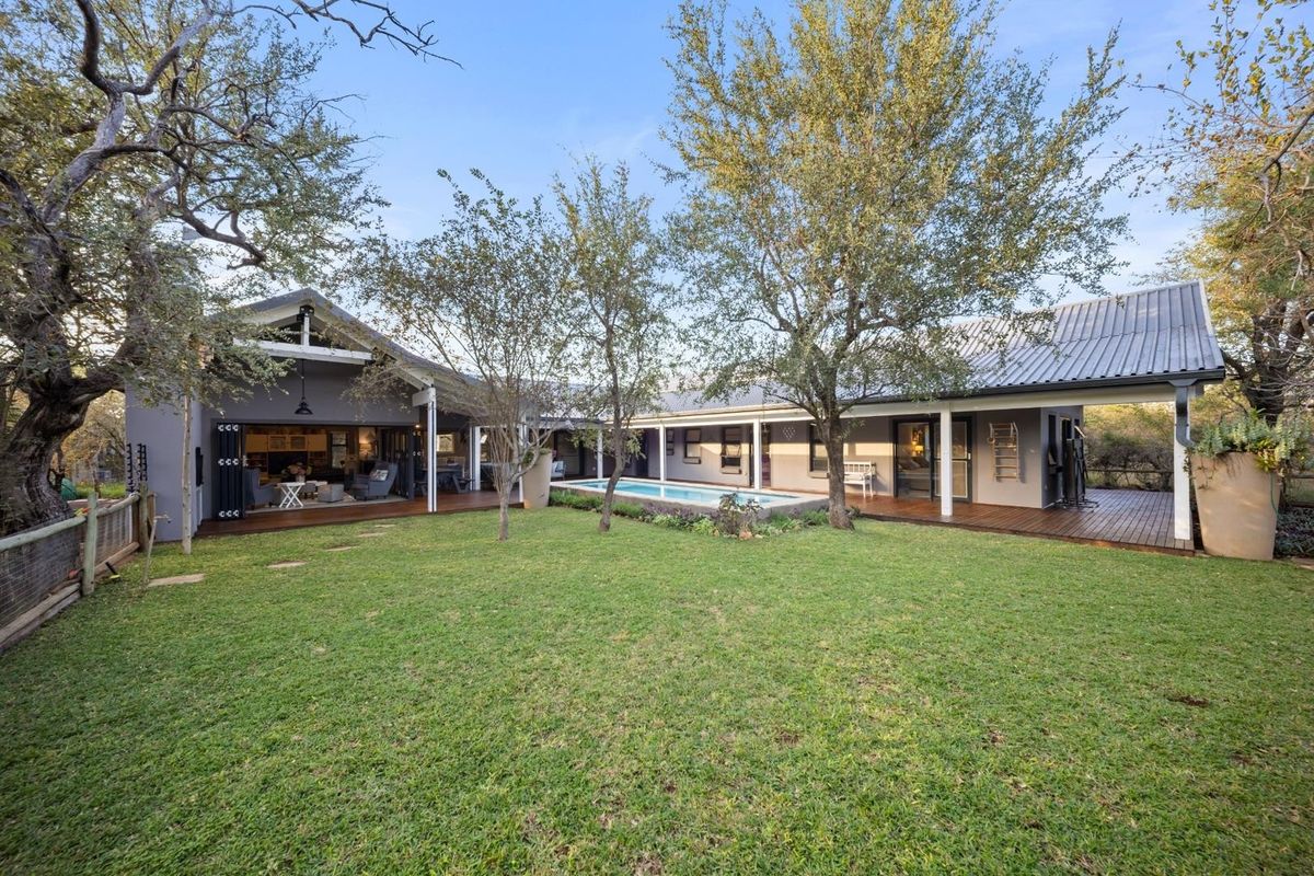 Spacious rear exterior featuring a well-maintained lawn, a swimming pool, and extensive timber decking connecting to the main house via large bi-fold doors.