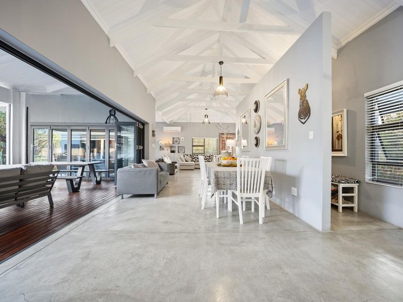 Spacious open-plan living and dining area featuring vaulted ceilings with exposed trusses, polished concrete floors, and seamless indoor-outdoor flow through large stacking glass doors.