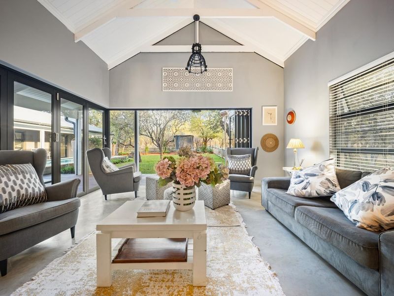 Spacious living room featuring a high vaulted ceiling with exposed rafters, polished concrete floors, and large bi-fold doors opening to the garden.