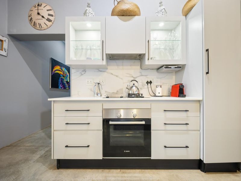 A modern, compact kitchen featuring white cabinetry, a built-in oven, cooktop, extractor fan, and a stylish marble-look splashback.