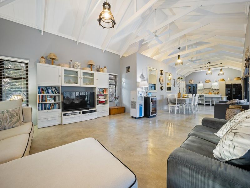Spacious open-plan living and dining area featuring high vaulted ceilings with exposed rafters, polished concrete floors, and integrated cabinetry.