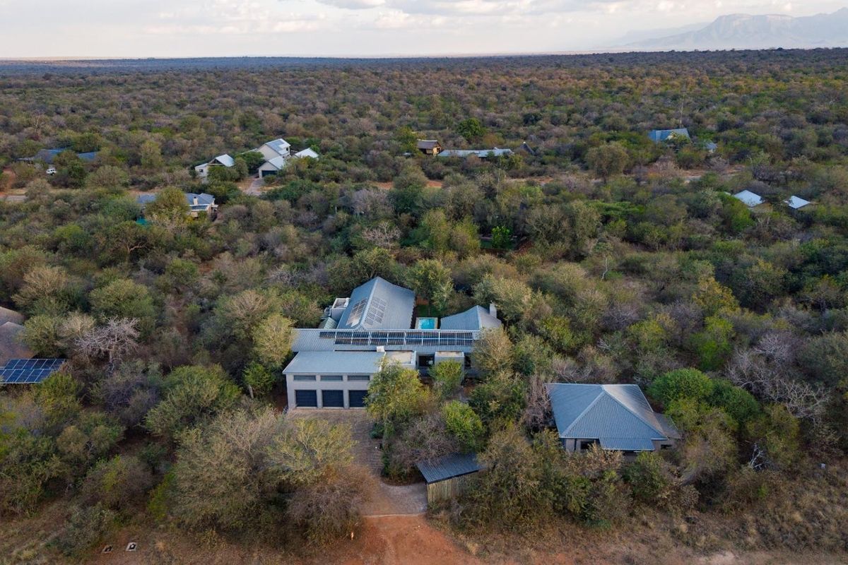 Aerial view of a modern residential property nestled in a wooded landscape, featuring solar panels, a swimming pool, and a multi-car garage.