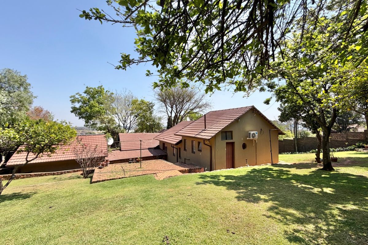 Rear view of the property featuring a tiled roof, brick patio area, and a spacious surrounding garden with mature trees.