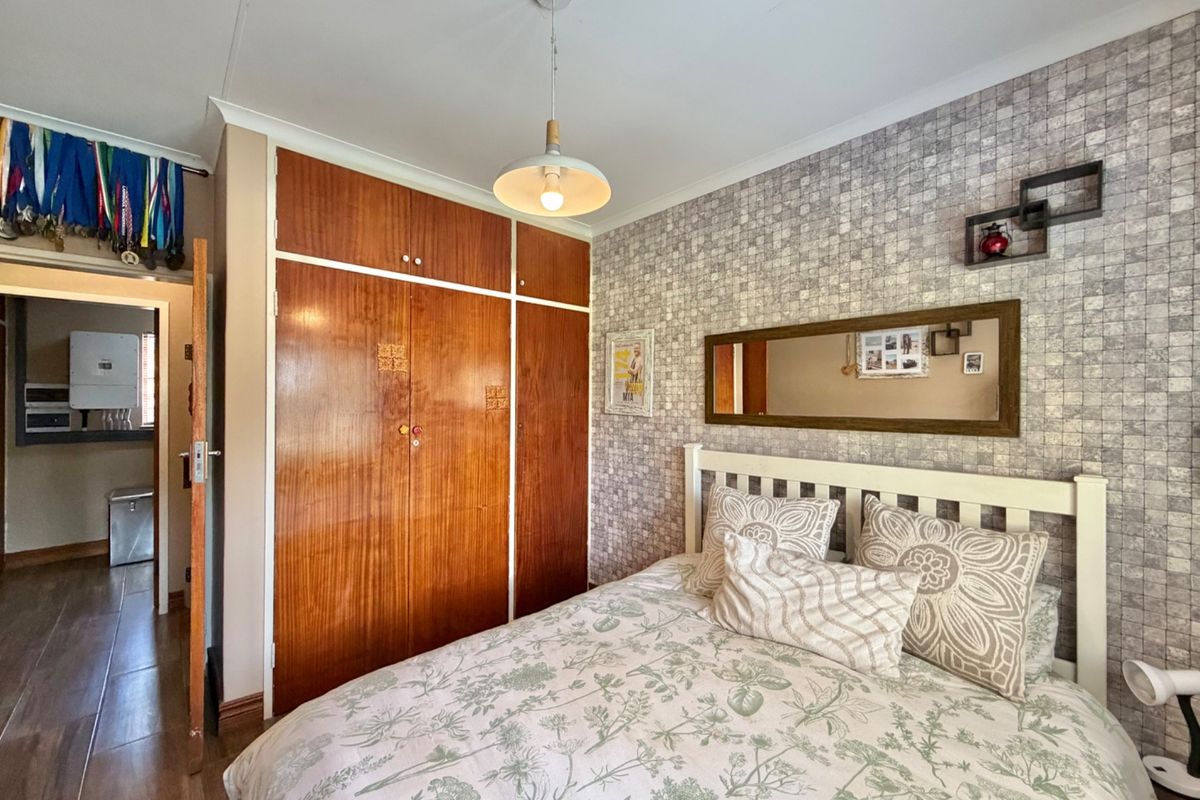 A bedroom featuring built-in wooden wardrobes, textured wallpaper, and laminate flooring, with a view into an adjacent hallway.