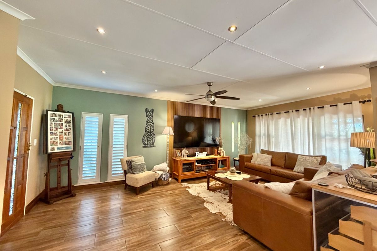 Spacious living room featuring timber-look floor tiles, a modern slatted timber feature wall, recessed downlights, and plantation shutters.