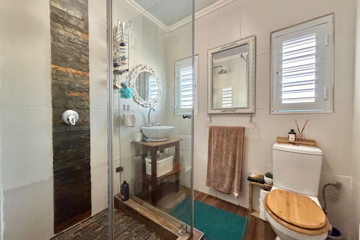 A well-maintained bathroom featuring a glass-enclosed shower with a stone accent wall, a vessel sink, and shutter-style windows.