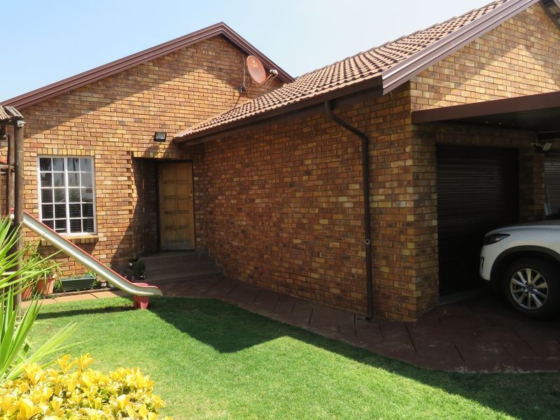 Front exterior view of a facebrick duet property featuring a garage, carport, and a small garden area.