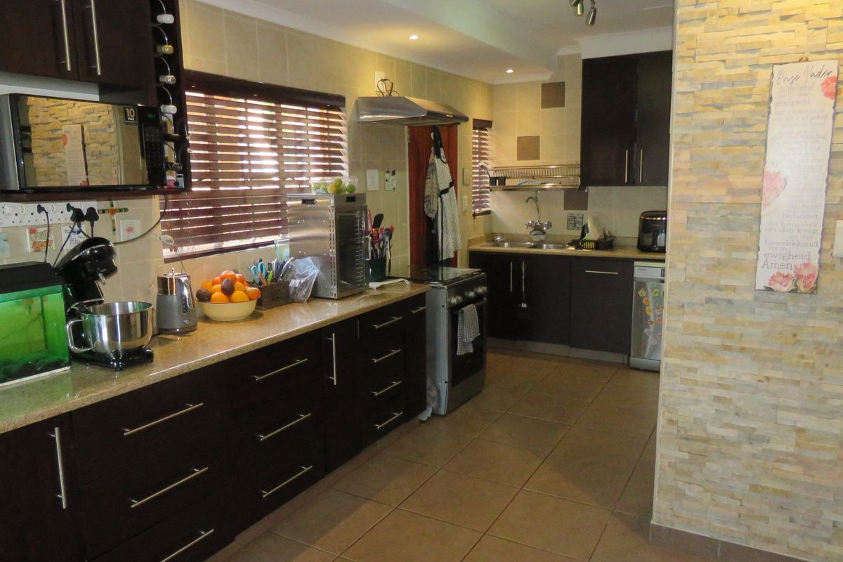 Functional kitchen featuring dark wood cabinetry, granite countertops, a stone-clad feature wall, and tiled flooring with integrated stainless steel appliances.