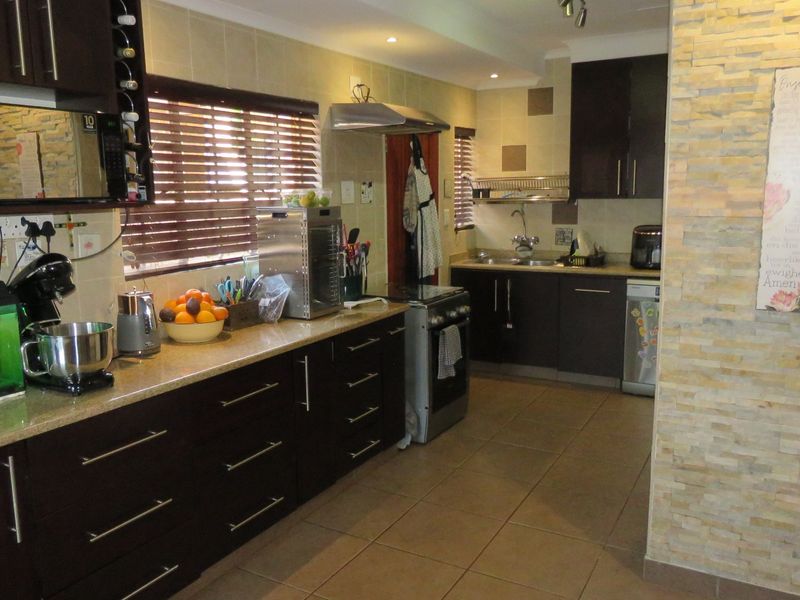 Functional kitchen featuring dark wood cabinetry, granite countertops, a stone-clad feature wall, and tiled flooring with integrated stainless steel appliances.