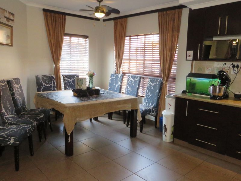 Open-plan kitchen and dining area featuring dark cabinetry, stone countertops, tiled flooring, and large windows with venetian blinds.