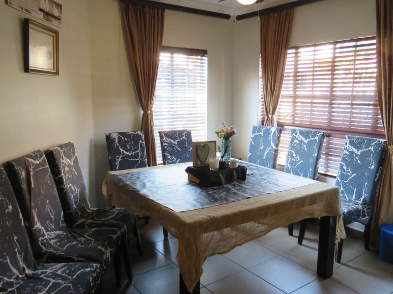 A functional dining room featuring tiled flooring, dual windows with venetian blinds, and a ceiling fan, providing a bright and practical space for meals.