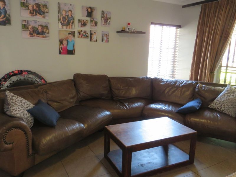 A comfortable living room featuring tiled flooring, large sliding glass doors with security gates, and venetian blinds, providing access to the outdoor area.