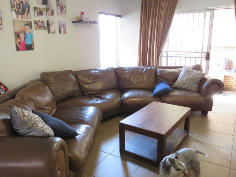 A living room featuring tiled flooring, large sliding glass doors with security gates, and venetian blinds, providing access to an outdoor area.
