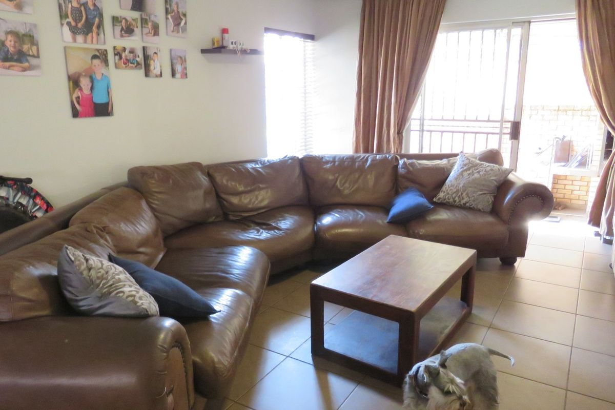 A living room featuring tiled flooring, large sliding glass doors with security gates, and venetian blinds, providing access to an outdoor area.
