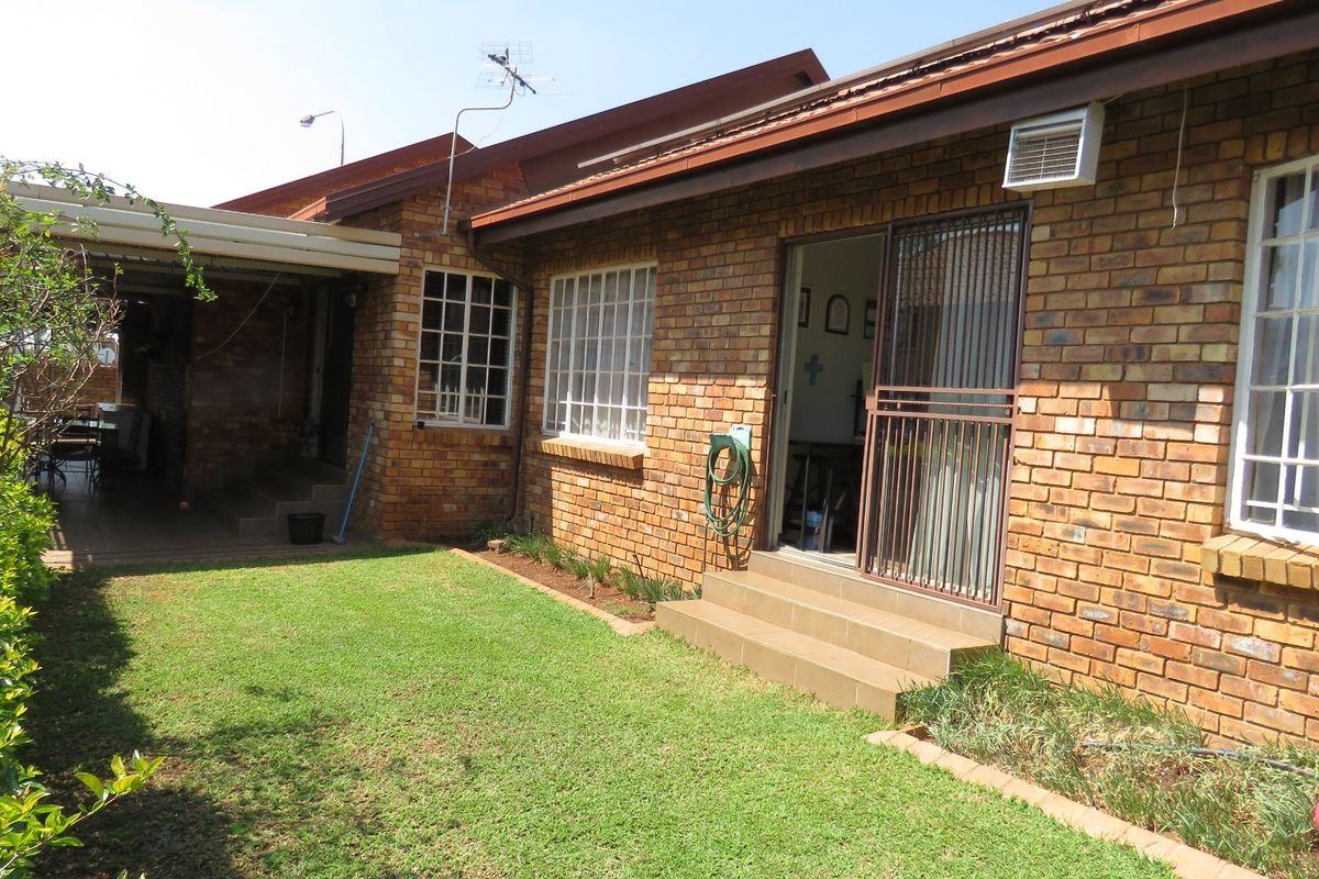 Rear view of the duet property featuring a face brick facade, covered patio area, and a private garden space.