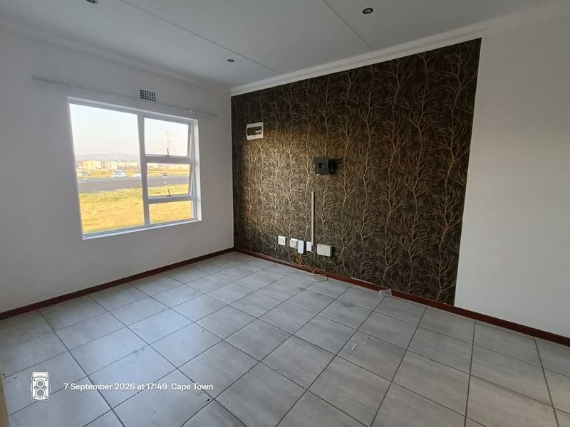 An empty living room featuring tiled flooring, a decorative feature wall, and large windows providing natural light and exterior views.