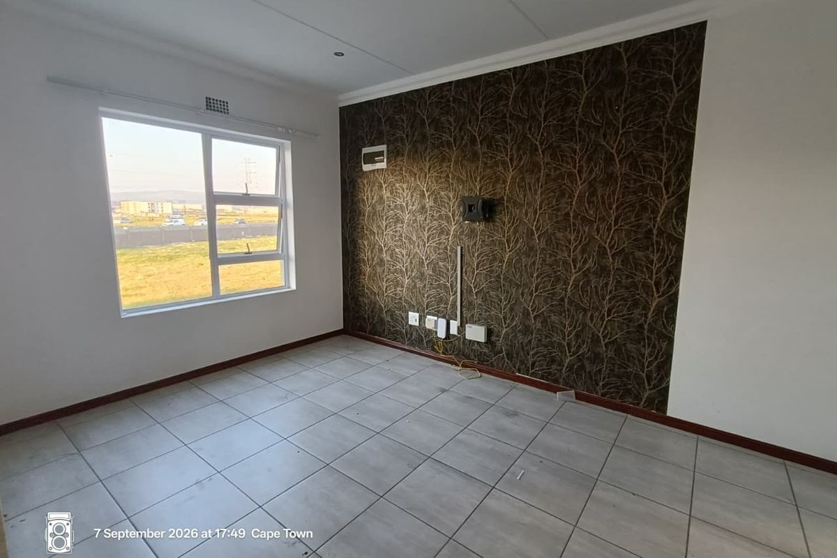 An empty living room featuring tiled flooring, a decorative feature wall, and large windows providing natural light and exterior views.
