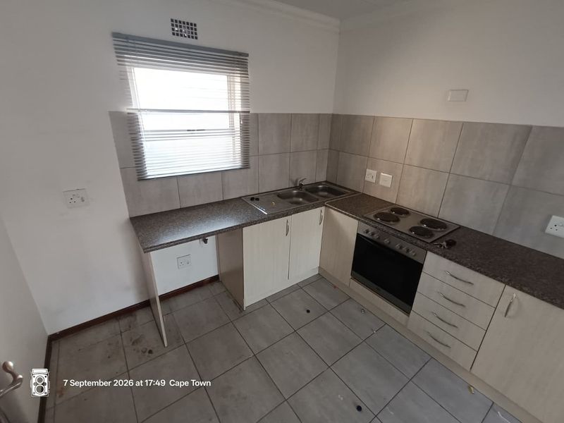 A functional kitchen featuring laminate cabinetry, built-in oven and hob, tiled backsplash, and tiled flooring. The space is currently vacant and ready for updates.