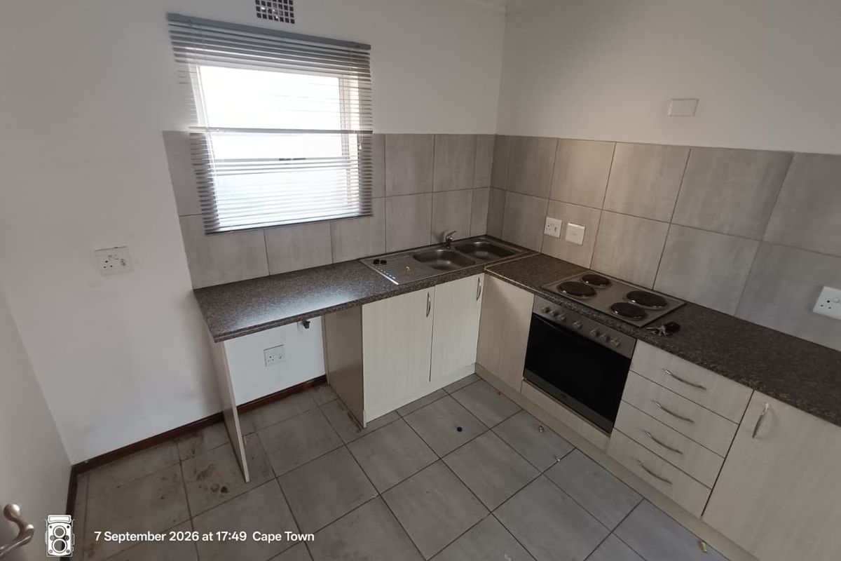A functional kitchen featuring laminate cabinetry, built-in oven and hob, tiled backsplash, and tiled flooring. The space is currently vacant and ready for updates.