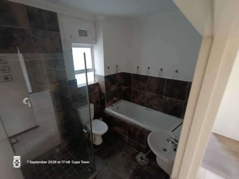 A functional bathroom featuring a glass shower enclosure, built-in bathtub, pedestal basin, and toilet with dark tiled finishes.