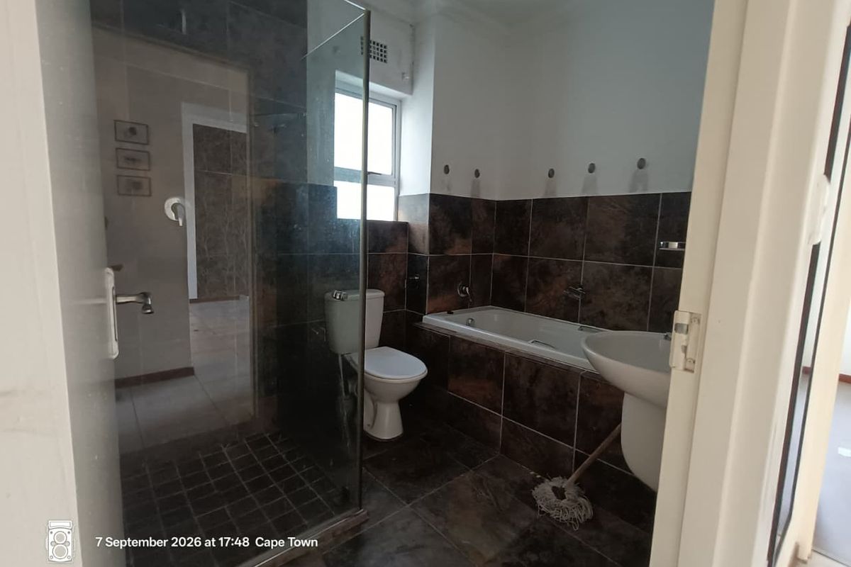 A functional bathroom featuring a glass shower enclosure, built-in bathtub, pedestal basin, and toilet with dark tiled finishes throughout.