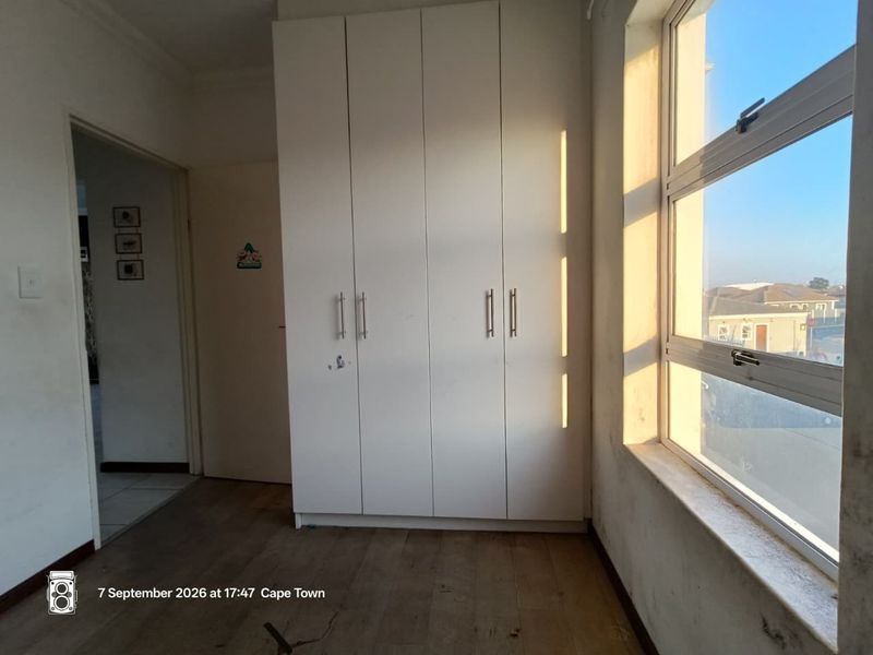 A bright, empty bedroom featuring built-in cupboards, laminate flooring, and large aluminium windows with natural light.
