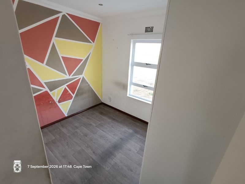 An empty bedroom featuring laminate flooring, an aluminium window, and a geometric painted feature wall in need of cosmetic refreshment.