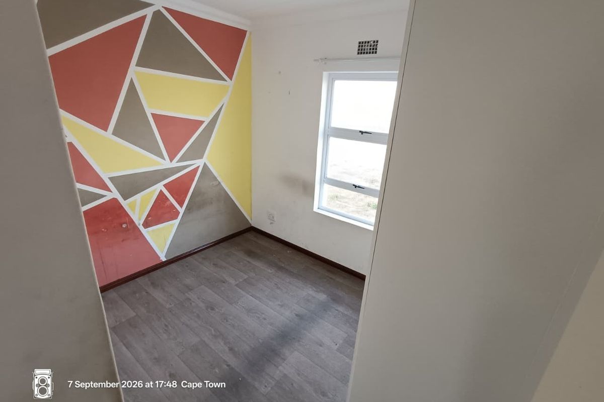 An empty bedroom featuring laminate flooring, an aluminium window, and a geometric painted feature wall in need of cosmetic refreshment.