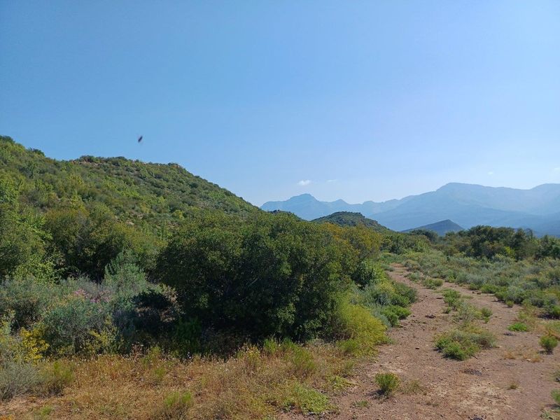 A scenic view of the natural landscape featuring rolling hills, native vegetation, and distant mountain ranges with a dirt access track.