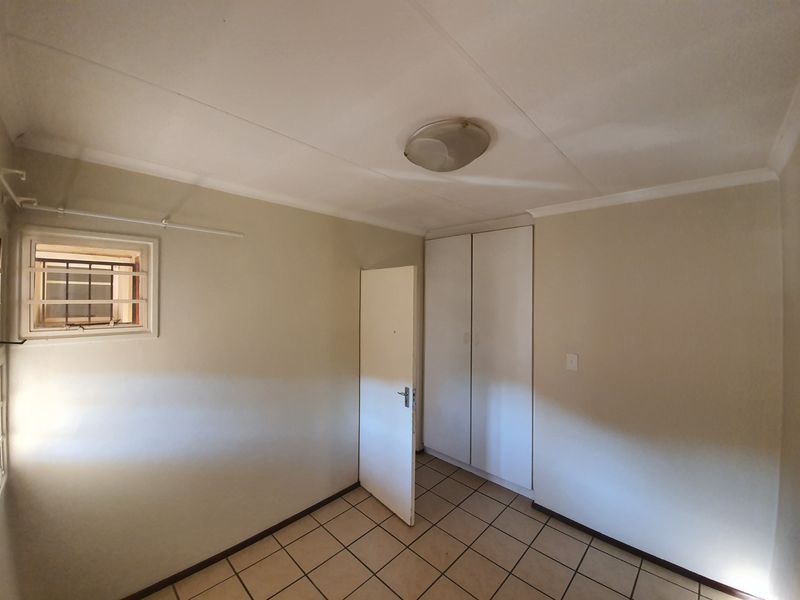 A clean, empty bedroom featuring neutral tiled flooring, built-in cupboards, and security bars on the window, offering a blank canvas for personalization.
