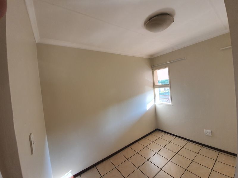 A clean, empty bedroom featuring neutral wall paint, tiled flooring, and a window with a curtain rail, ready for personalization.
