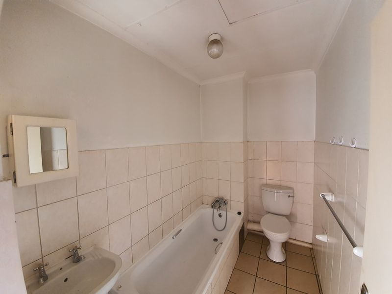 A dated bathroom featuring a standard bathtub, pedestal basin, and toilet with neutral wall and floor tiling, ready for modernization.