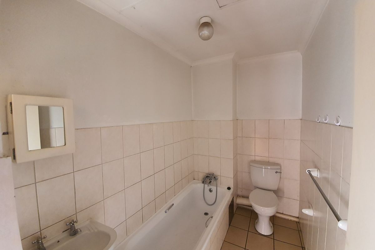 A dated bathroom featuring a standard bathtub, pedestal basin, and toilet with neutral wall and floor tiling, ready for modernization.