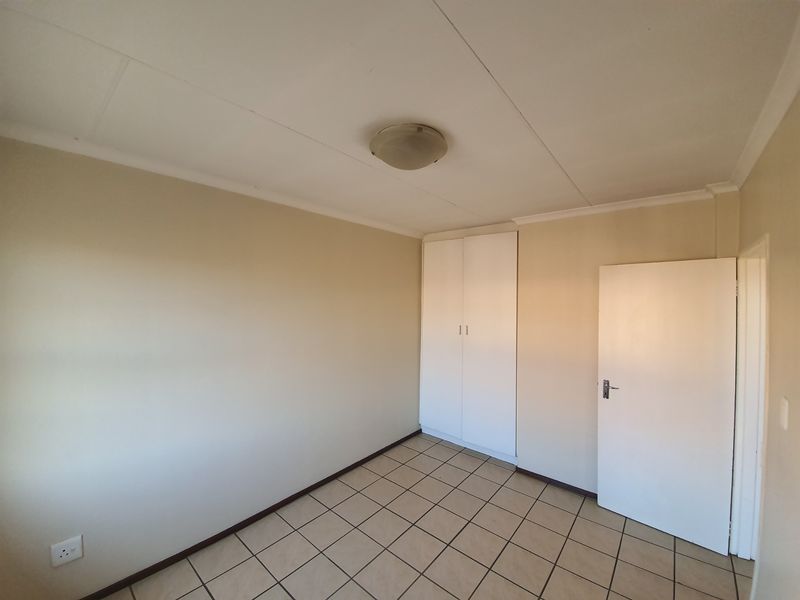 A clean, empty bedroom featuring neutral wall tones, tiled flooring, and a built-in wardrobe, offering a blank canvas for personalization.