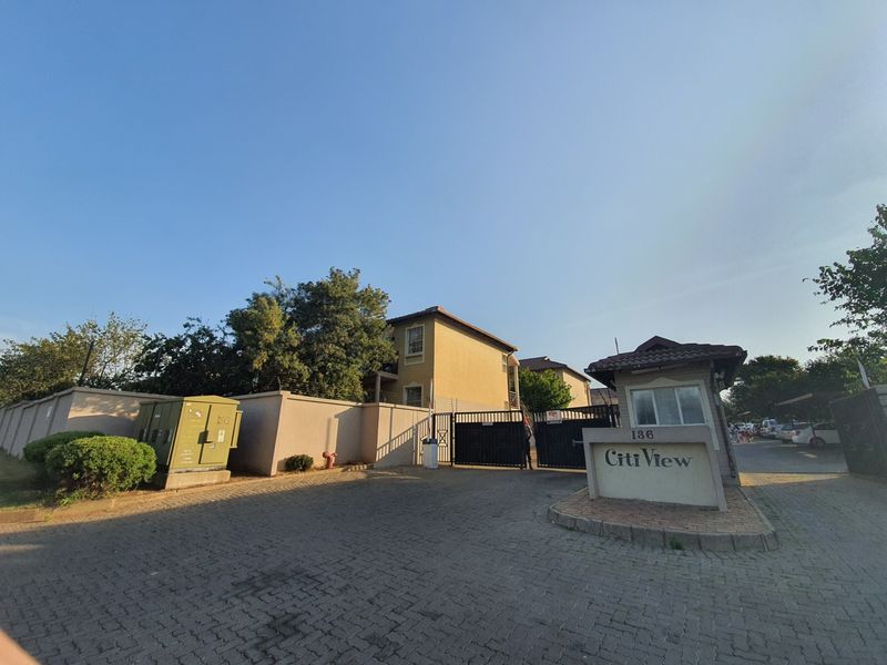 The entrance to Citi View townhouse complex featuring a secure gated access point, guard house, and paved driveway.