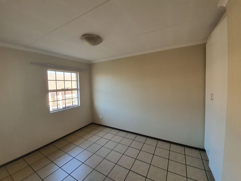 A clean, empty bedroom featuring neutral walls, tiled flooring, and a built-in cupboard, offering a blank canvas for personalization.