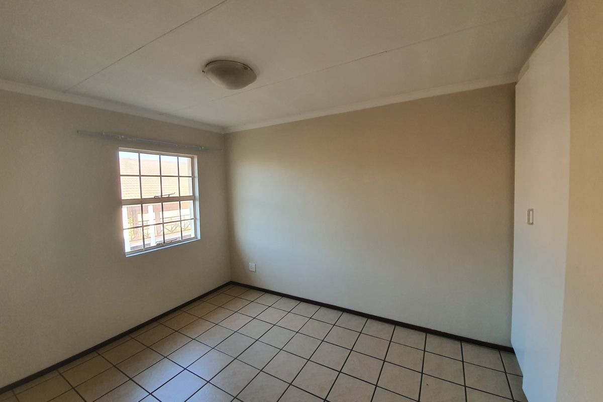 A clean, empty bedroom featuring neutral walls, tiled flooring, and a built-in cupboard, offering a blank canvas for personalization.
