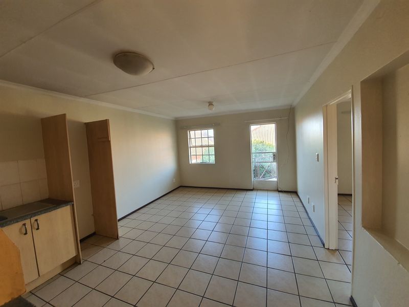 An open-plan living and kitchen area featuring tiled flooring, built-in cabinetry, and natural light from windows and a door leading to a balcony.