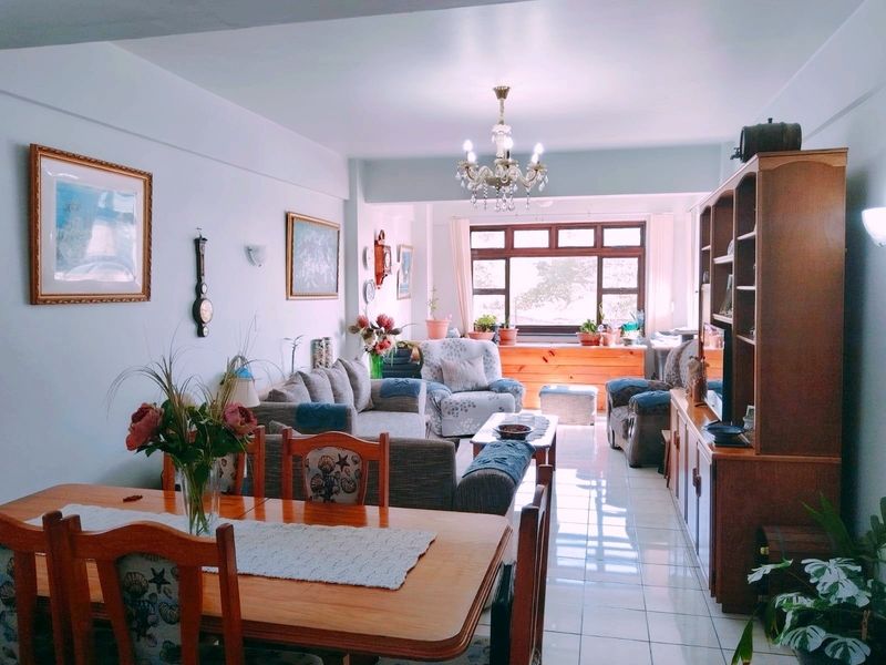 An open-plan living and dining area featuring tiled flooring, a central chandelier, and large timber-framed windows allowing for natural light.
