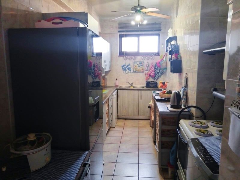 A functional galley-style kitchen featuring tiled walls and flooring, built-in cabinetry, and a double basin sink.