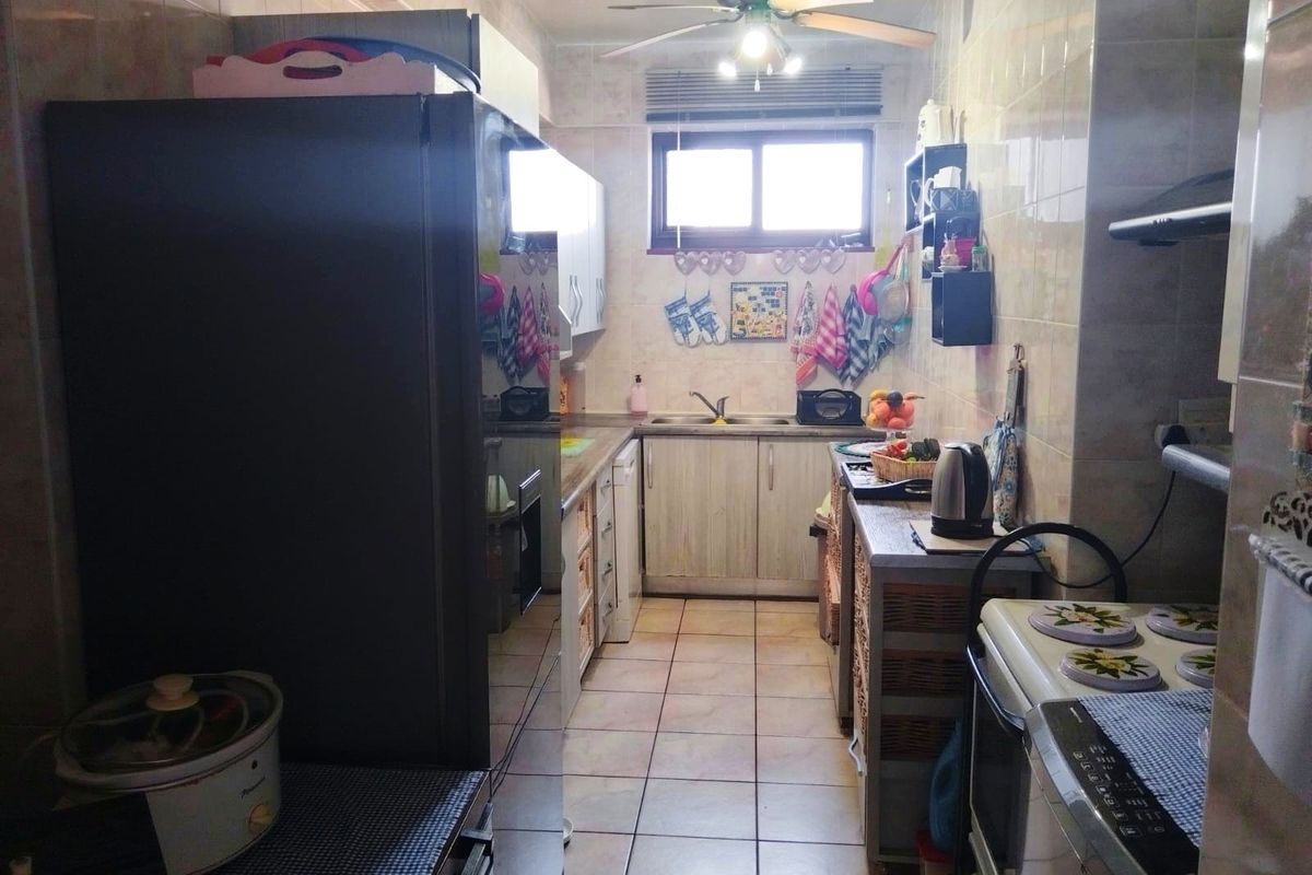 A functional galley-style kitchen featuring tiled walls and flooring, built-in cabinetry, and a double basin sink.