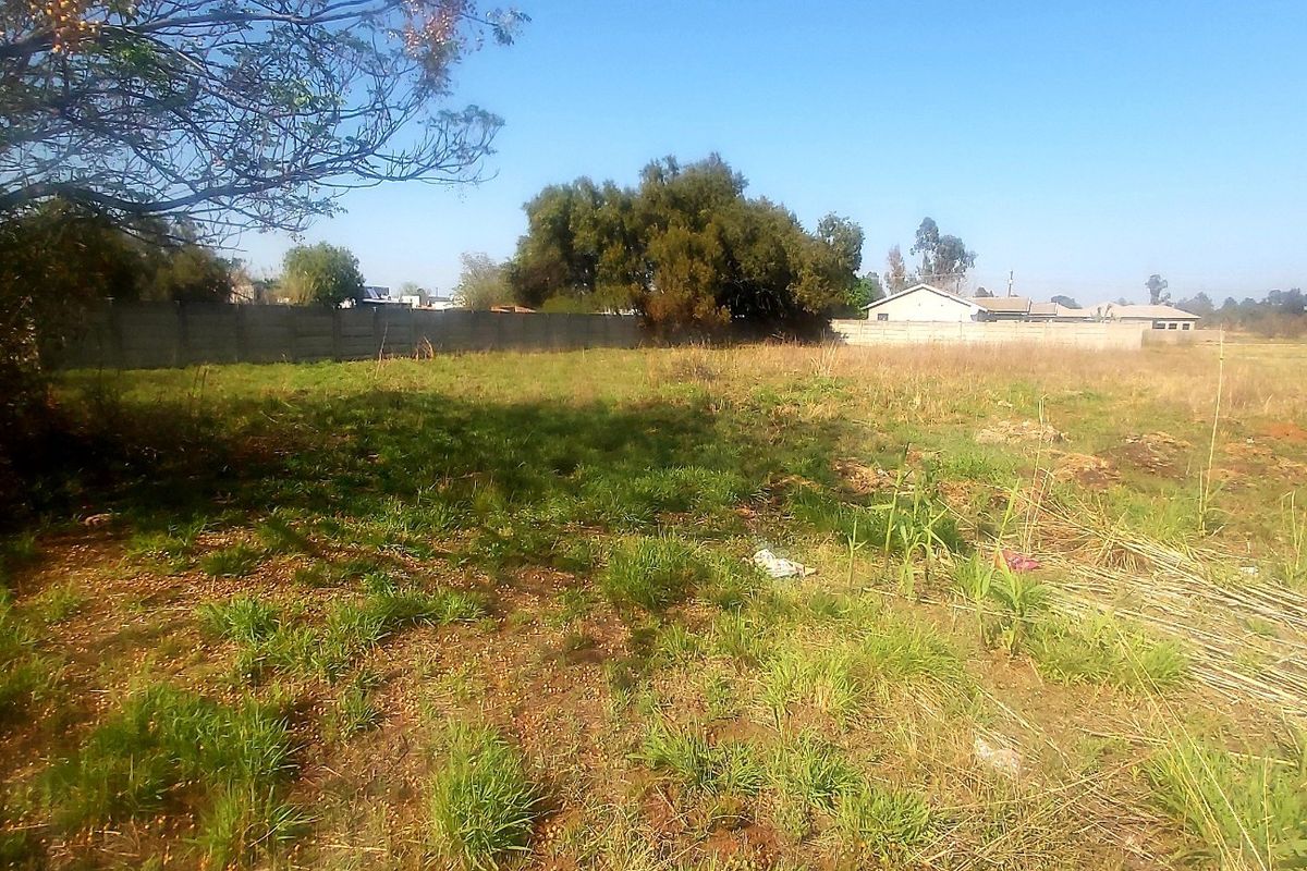 A view of a vacant residential plot featuring natural grass coverage and a precast concrete boundary wall along the perimeter.