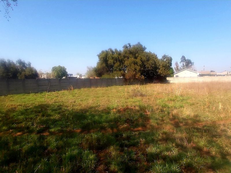 A vacant residential plot featuring a precast concrete boundary wall and natural grass coverage.